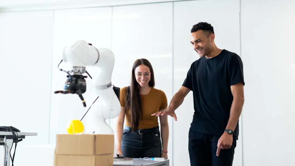 Two professionals smiling while interacting with a modern robotic arm in a brightly lit lab.