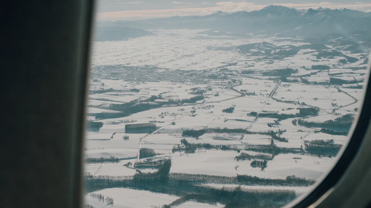 A snowy landscape and distant mountain ranges viewed through the oval window of a passenger airplane.