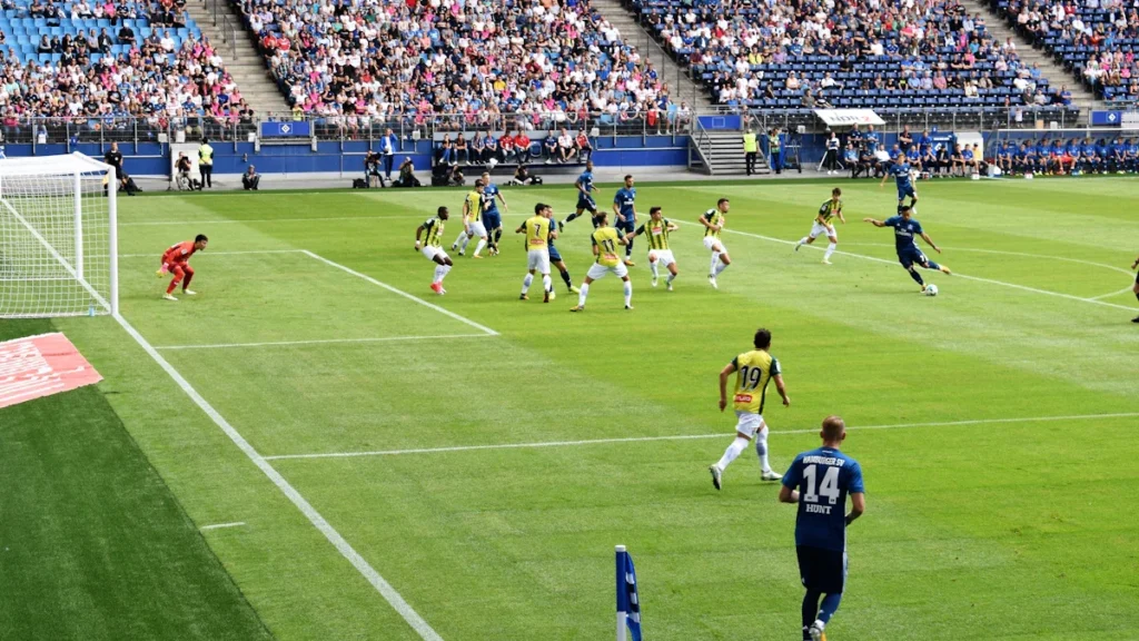Action shot of a professional soccer match in a crowded stadium with players competing near the goal.