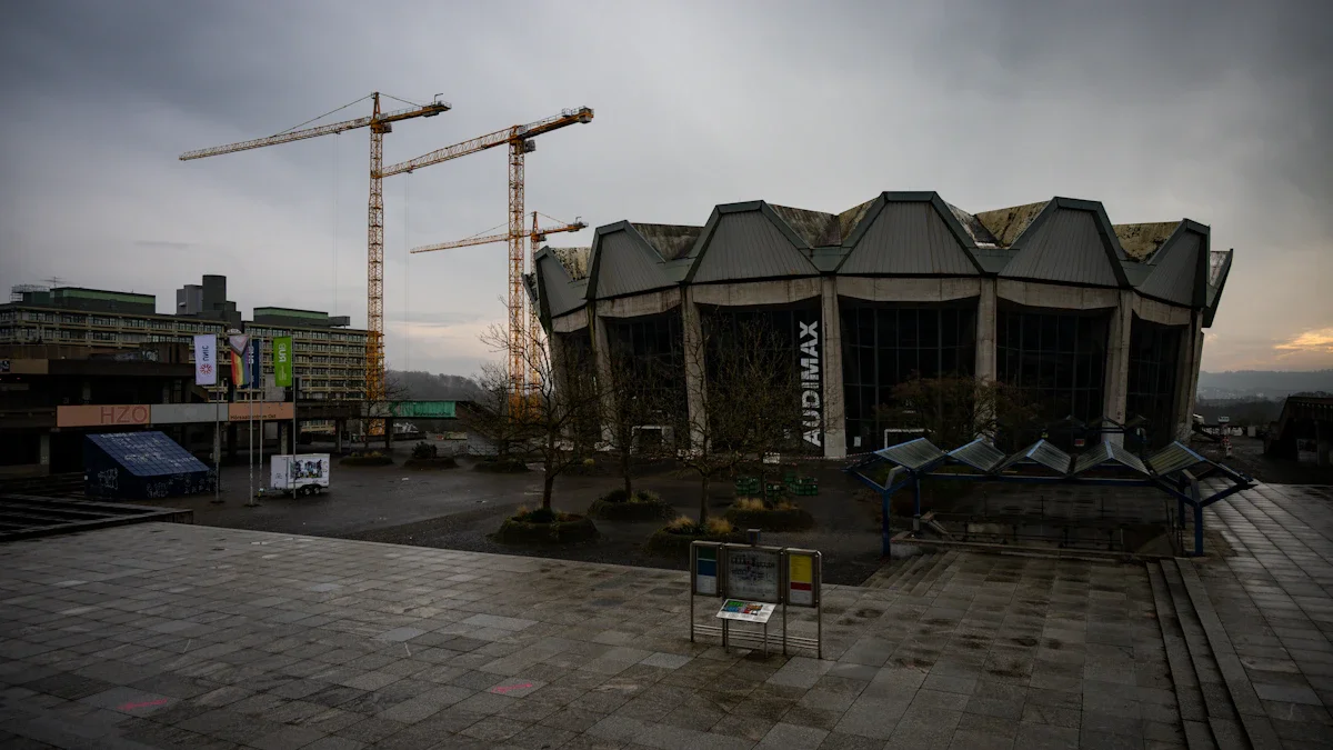 A large construction site featuring multiple cranes over a modern brutalist building under an overcast sky.