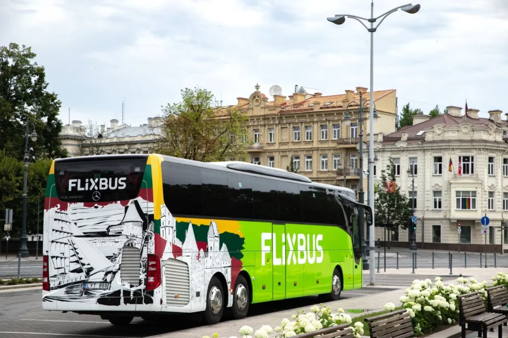 A bright green FlixBus with Lithuanian themed graphics parked on a city street near buildings.
