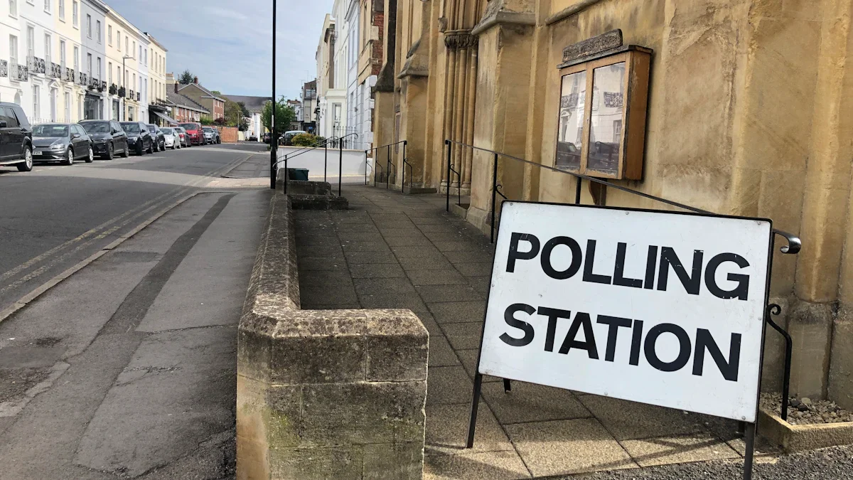 A white 'Polling Station' sign stands on a sidewalk outside a traditional stone building in a typical UK residential street.