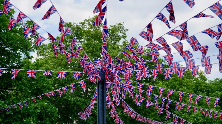 Strings of Union Jack bunting flags attached to a street pole against a bright cloudy sky.
