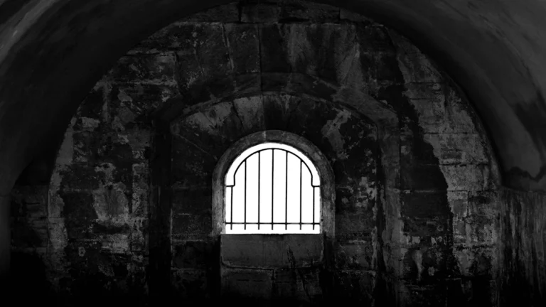 A black and white photograph of a small barred window inside a prison cell in Derby, UK.
