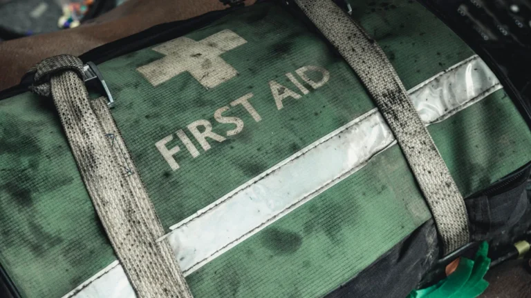 A weathered green and black first aid bag featuring a white cross and bold white text.