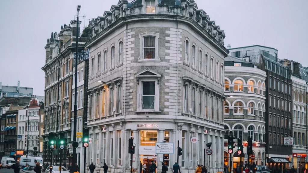 A multi-story stone building at a busy London street corner with pedestrians and traffic lights.