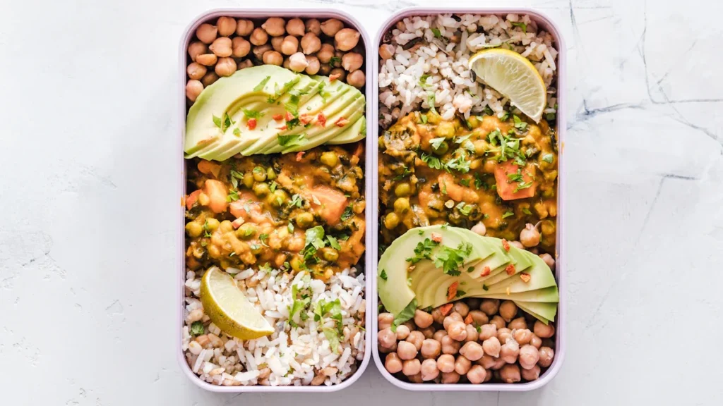 Balanced meal prep containers featuring grilled chicken, lemon slices and fresh mixed greens.