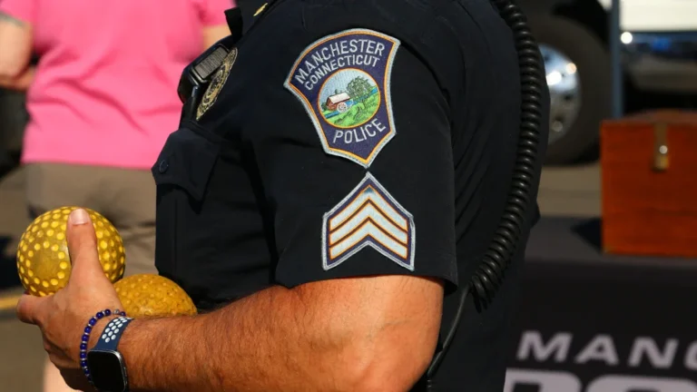 Close-up of a police officer's arm with a Manchester Connecticut patch, holding two yellow balls.