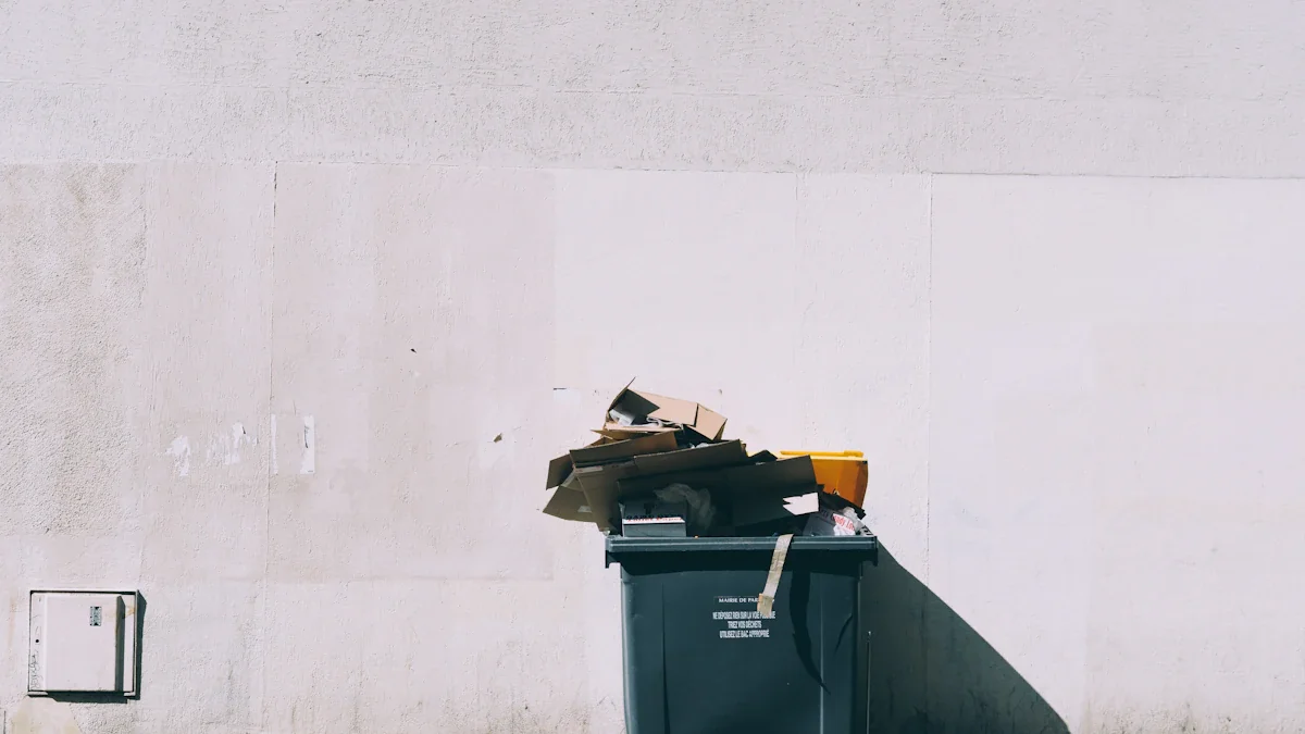 A standard black household waste bin on wheels against a white wall.