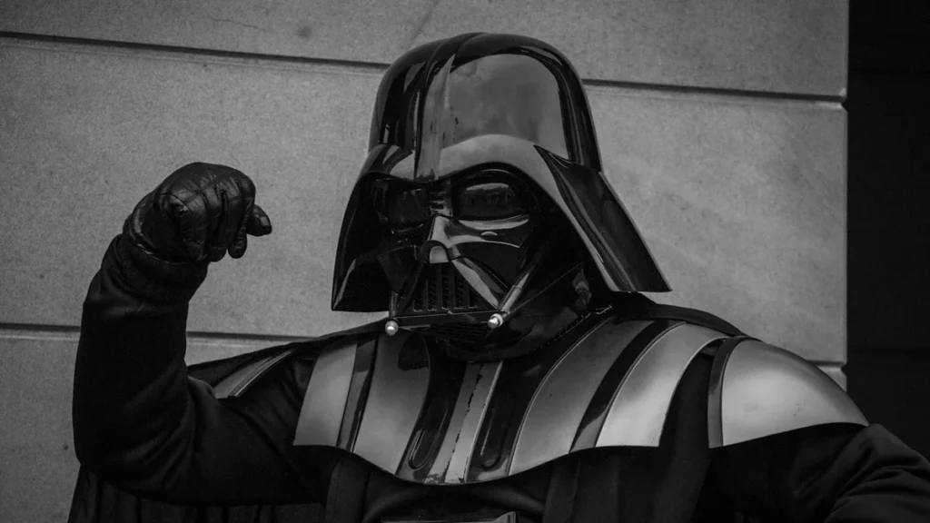 A person in a Darth Vader costume raises a fist, symbolizing the physical presence and strength of actor David Prowse.