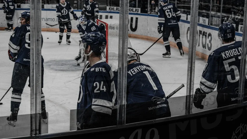 Ice hockey players in blue uniforms warming up on the ice rink behind a glass barrier.