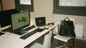 A modern white desk in Riga featuring a laptop and a monitor displaying a map of Latvia.