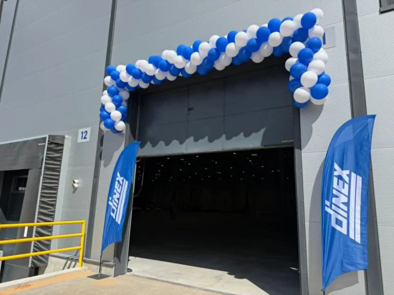 Blue and white balloon arch above a warehouse bay door flanked by two Dinex branded flags.