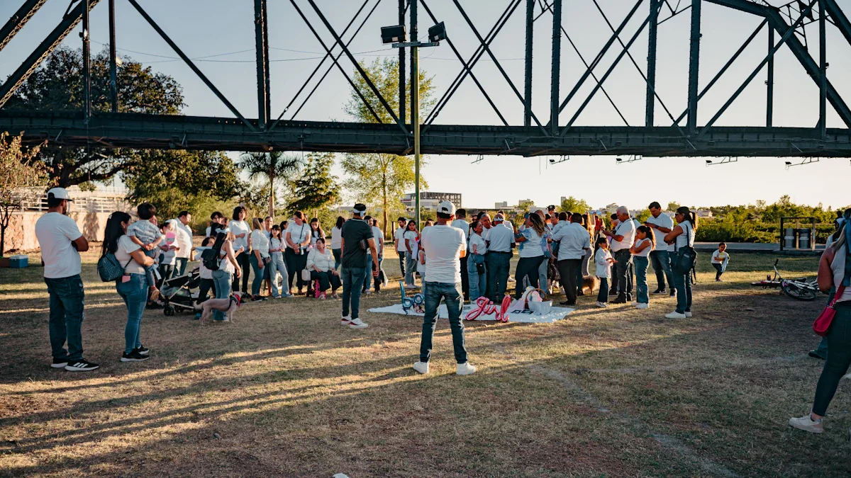 A large group of community members gathered under a steel bridge structure in Gunnersbury Park for a centenary celebration.