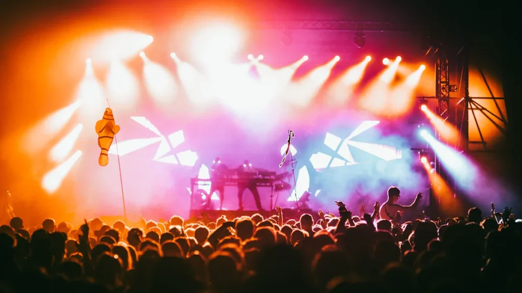 Crowd of people at a UK music festival watching a bright concert performance.