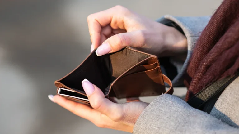 A close-up of a young person's hands with manicured nails holding open an empty brown leather wallet.