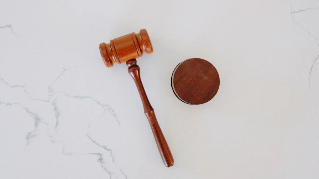 A wooden judge's gavel and sound block placed on a white marble background.