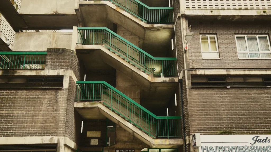 A London building with concrete stairwells, green railings, and a local hairdressing shop at street level.