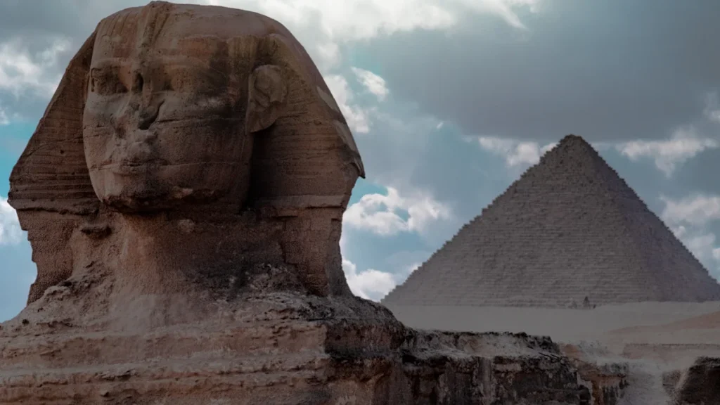 The Great Sphinx and a pyramid under a cloudy sky in Giza, Egypt.