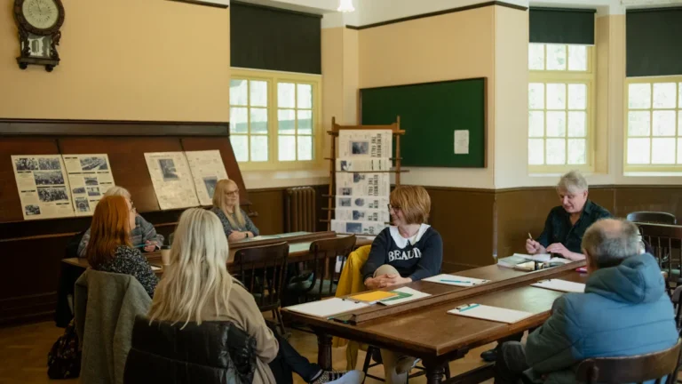 A diverse group of community members sitting at tables in a local meeting hall, reviewing planning documents and displays.