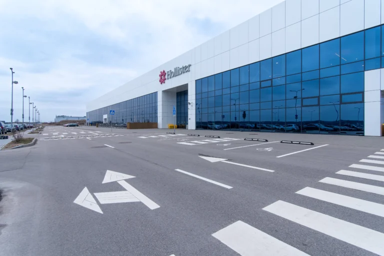 A large modern building with white panels, blue glass windows, and a red Hollister logo.