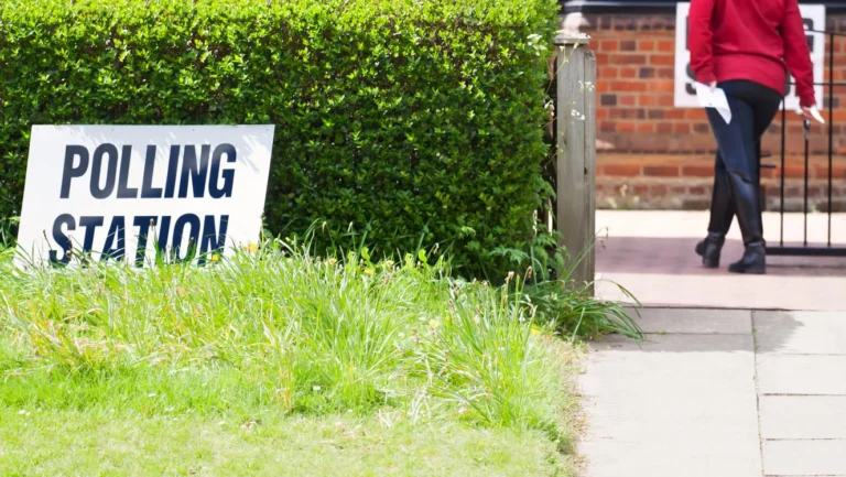 A white 'POLLING STATION' sign in grass with a person walking away in the background.