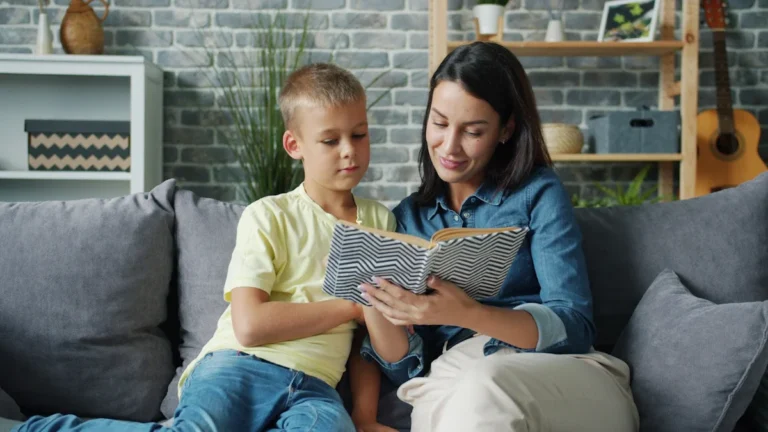 A supportive foster mother and young boy reading a book together on a comfortable sofa in a cozy living room.