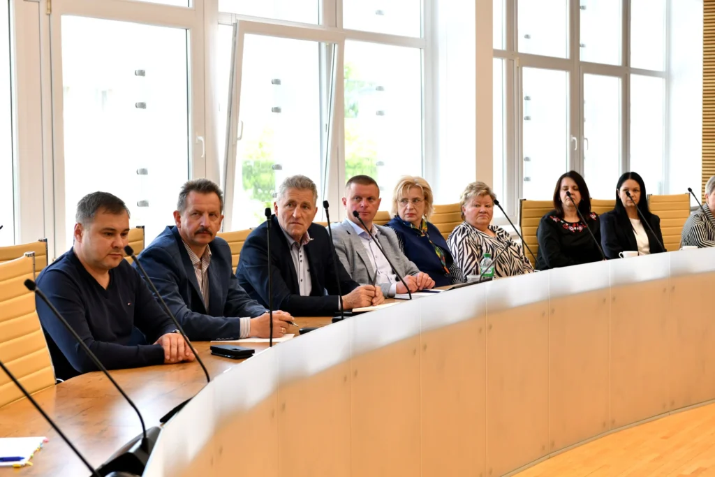 Professionals sitting at a curved conference table with microphones in a bright, modern meeting room.