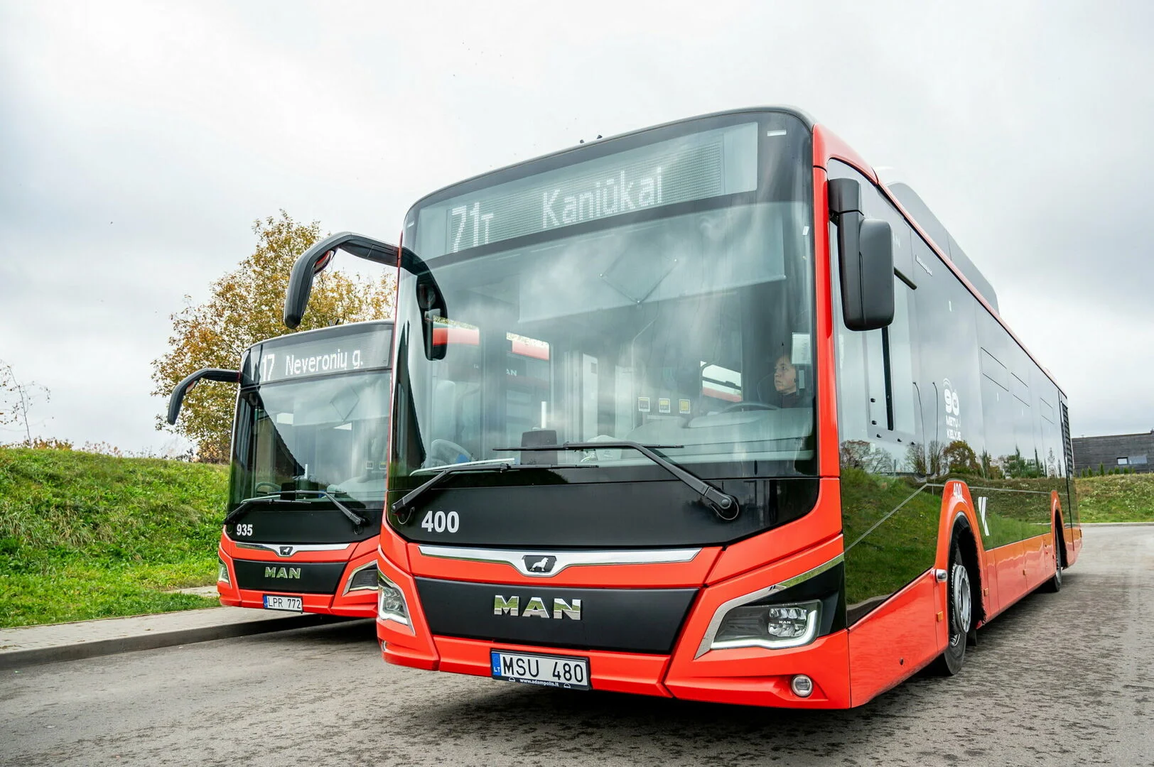 Two modern red and black MAN city buses parked side-by-side on an overcast day.