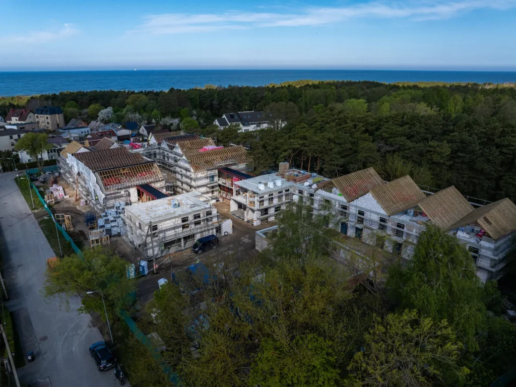 Aerial view of multi-story buildings under construction with scaffolding near a forest and the sea.