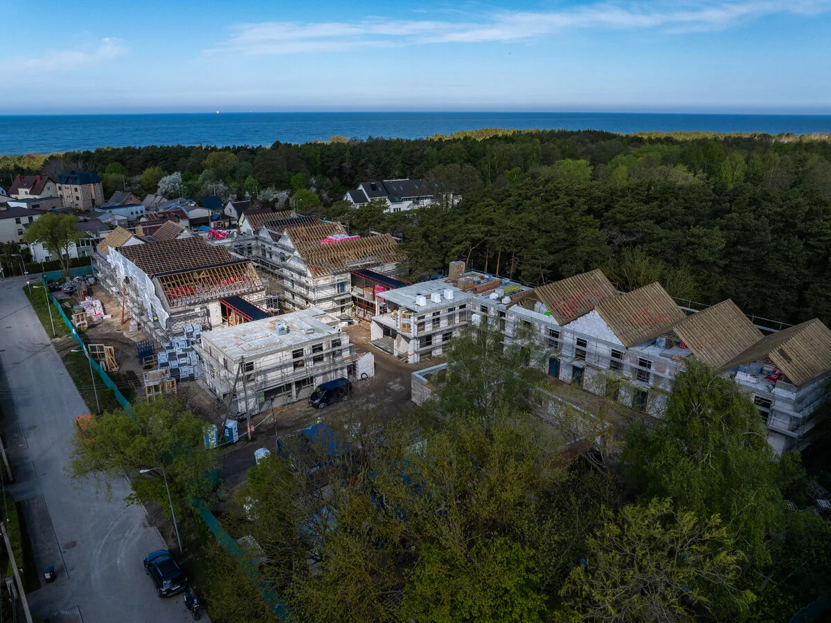 Aerial view of multi-story buildings under construction with scaffolding near a forest and the sea.
