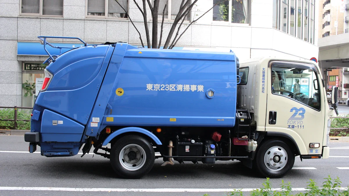 A blue industrial waste collection truck driving along an urban road in a city setting.