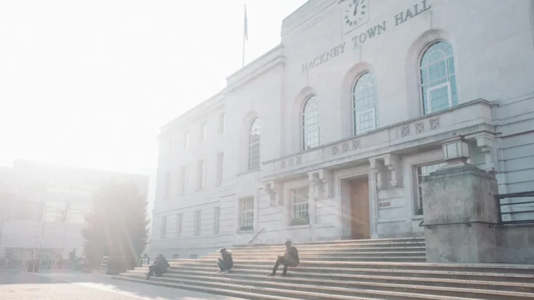 A bright, sun-drenched view of a classic stone Town Hall building with people sitting on the front steps, symbolizing local government and community services.
