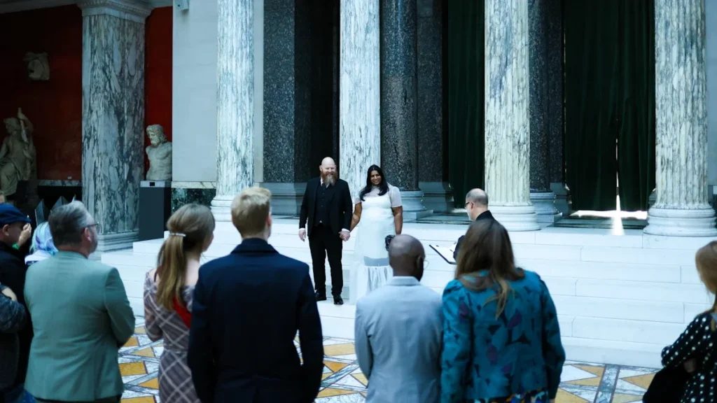 A large crowd of people gathered in a grand marble hall with classical columns for a meeting.