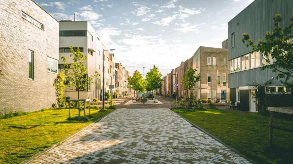 A modern brick-paved residential walkway in the UK with green grass and young trees.