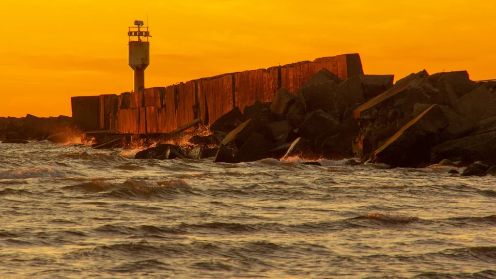 A white lighthouse stands against a vibrant orange sunset over the Baltic Sea in Liepāja, Latvia.