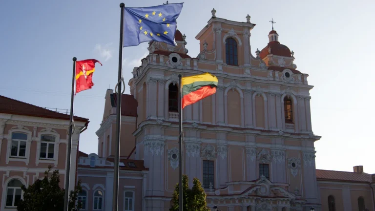 The ornate pink facade of St. Casimir's Church in Vilnius with Lithuanian and European Union flags.