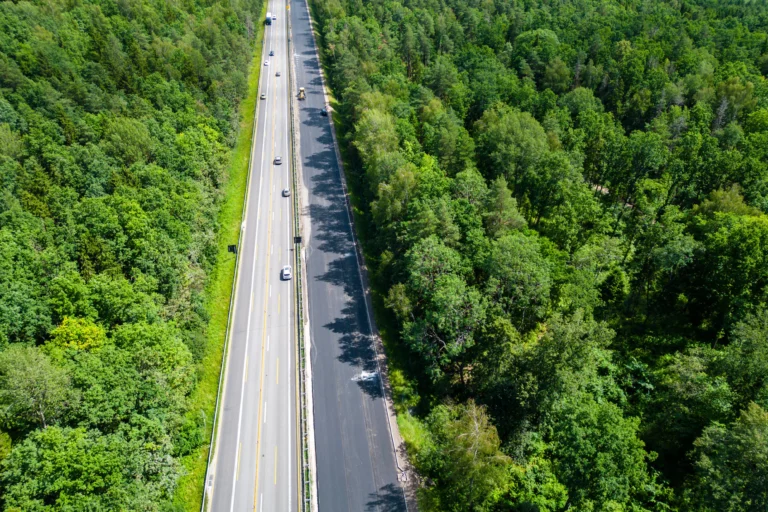 Aerial view of cars driving on a multi-lane highway through a dense green forest.