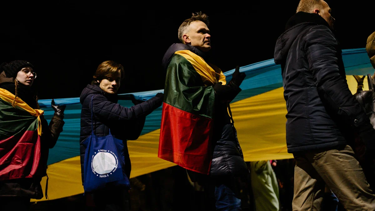 A man wearing a Lithuanian flag stands alongside others holding a giant Ukrainian flag at night.