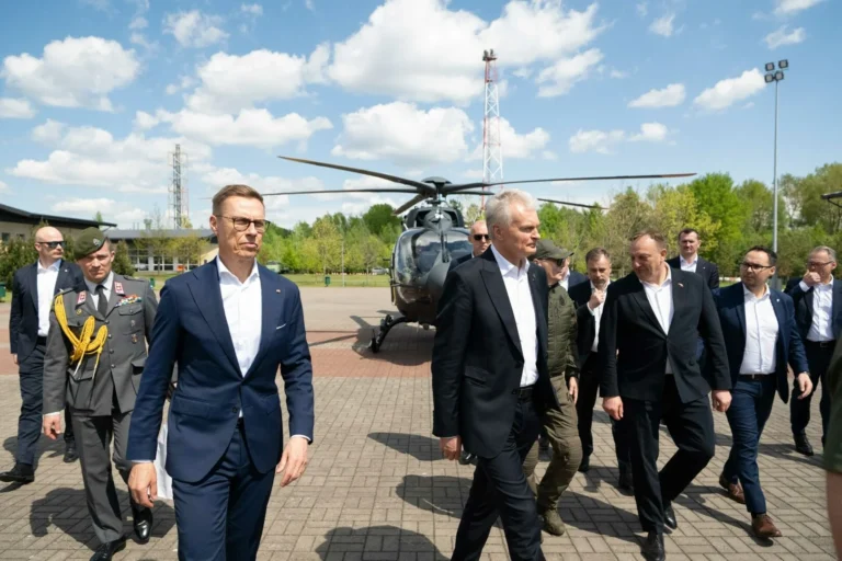 Several men in suits and military uniform walking outdoors with a helicopter in the background.
