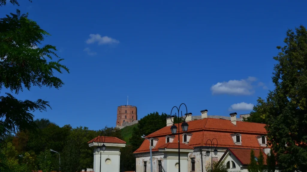 White manor building with a red roof beneath the historic Gediminas Castle Tower in Vilnius, Lithuania.