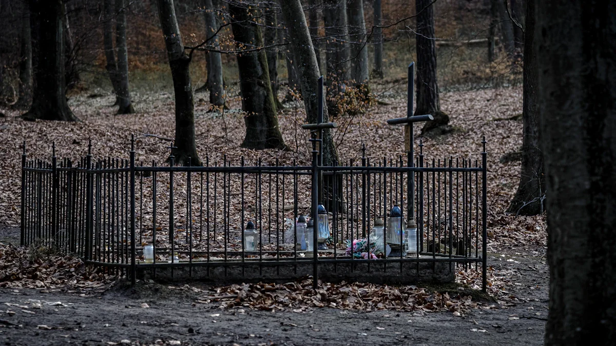 A solemn grave enclosed by a black metal fence with crosses in a quiet, leaf-strewn forest.