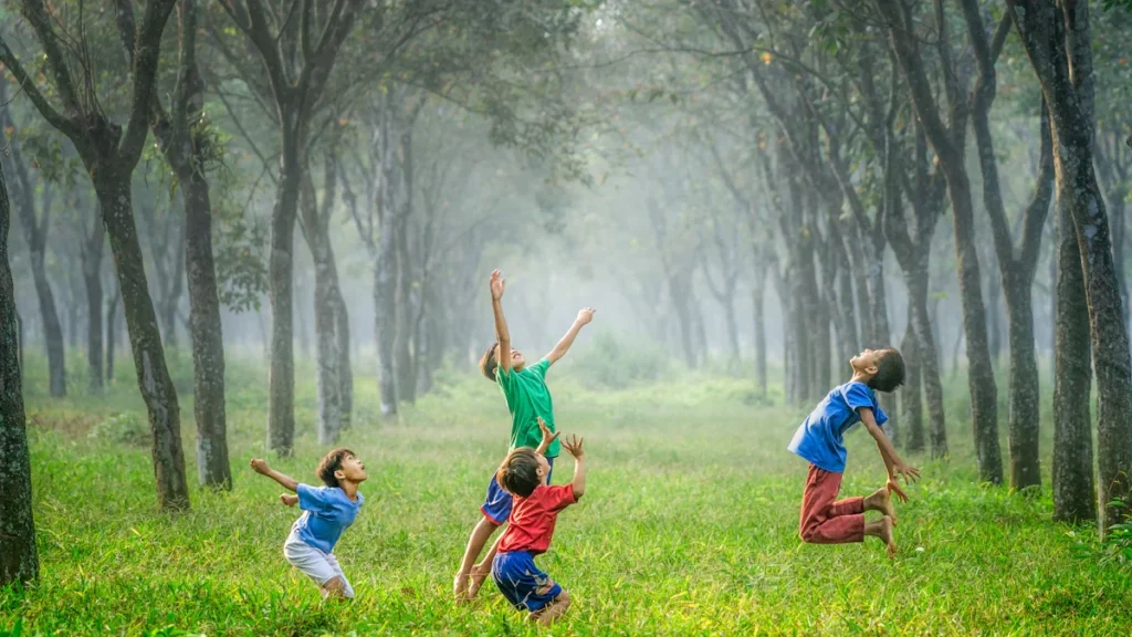 Four children playing with a ball in a misty green park surrounded by tall trees.