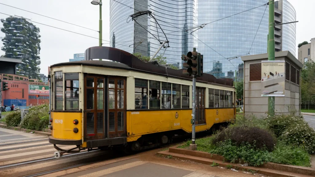 A classic yellow tram car traveling along city tracks with modern glass skyscrapers in the background.