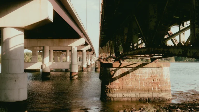 A low-angle shot showing the concrete support pillars and underside of two parallel bridges over water.