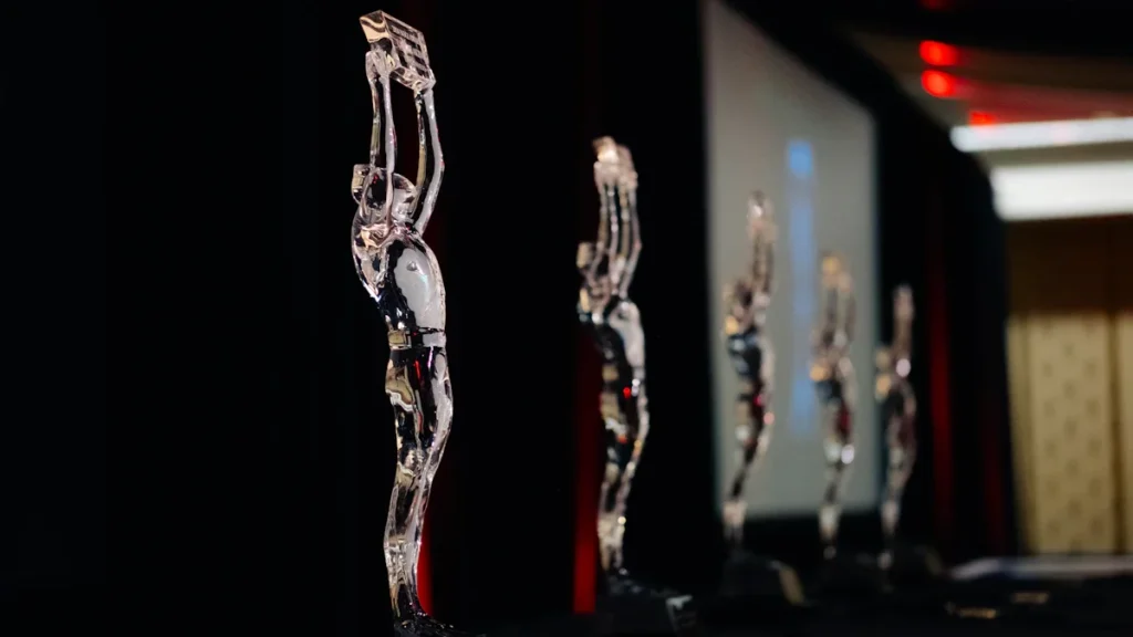 A row of elegant clear glass statuettes shaped like human figures on a dark stage.