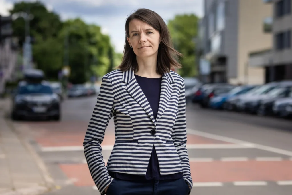 Woman wearing a blue and white striped blazer stands on a blurred urban street.