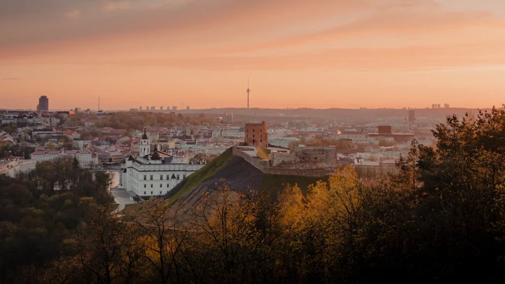Panoramic sunset view over Vilnius, Lithuania, showing the Palace of the Grand Dukes and city landmarks.