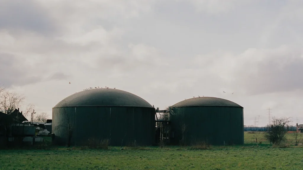 Two large green circular biomethane storage tanks situated in a grassy European field.