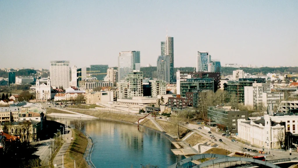 A skyline view of Vilnius, Lithuania, featuring modern office buildings and the Neris river, representing the country's economic growth.